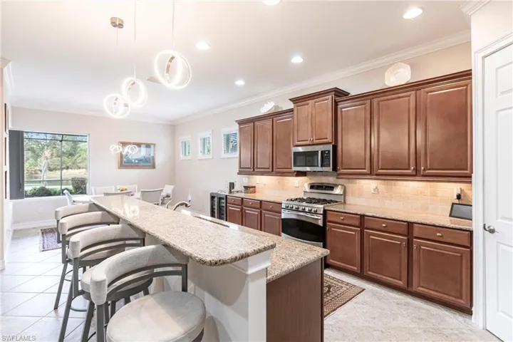Kitchen with a lot of natural light, upgraded light fixtures, under cabinet lighting, appliances with stainless steel finishes, and a breakfast bar area