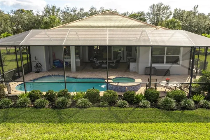 View of back of house with swimming pool with an in ground hot tub, extended a lanai and outdoor kitchen on a large lot.