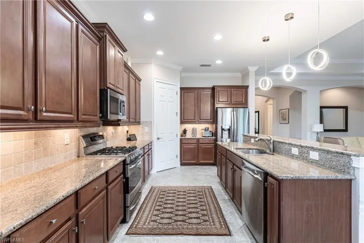 Kitchen featuring decorative backsplash, stainless steel appliances, crown molding, sink, and hanging light fixtures