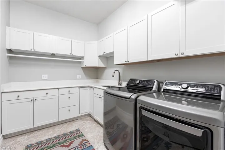 Laundry area with cabinets, light tile patterned flooring, washing machine and dryer, and sink
