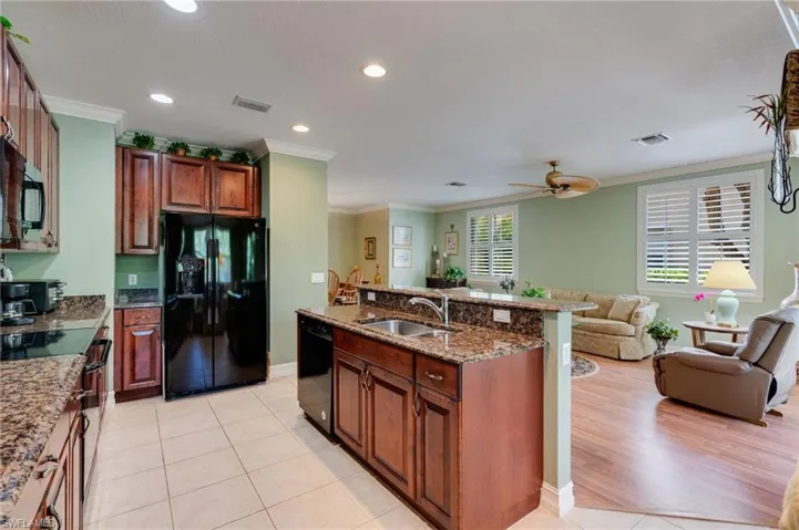 Kitchen with black appliances, light stone counters, open floor plan, an island with sink, and crown molding