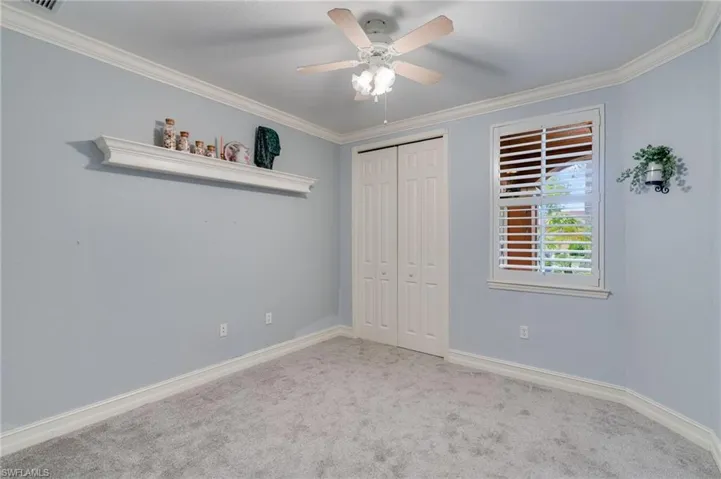 Unfurnished bedroom featuring light carpet, ornamental molding, a closet, and a ceiling fan