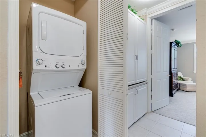 Laundry area with stacked washing machine and dryer and light tile patterned floors