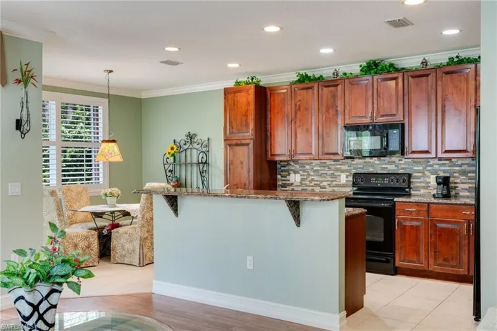 Kitchen with black appliances, light stone counters, hanging light fixtures, decorative backsplash, and crown molding