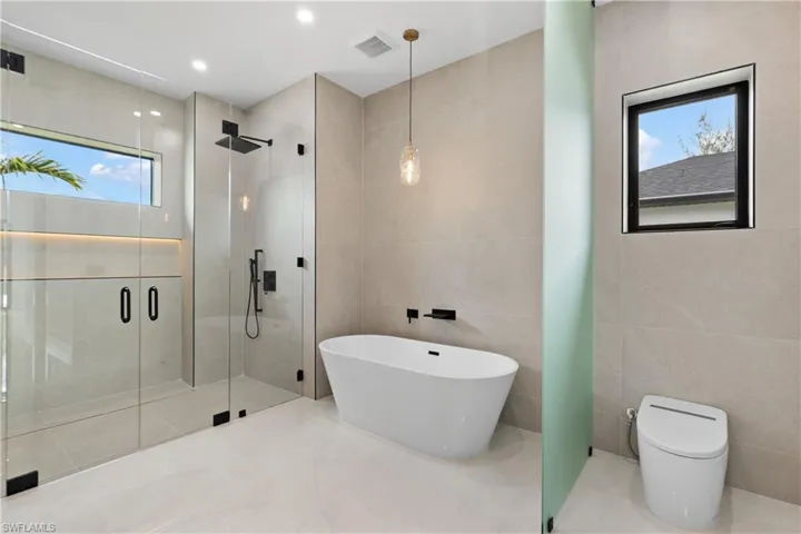 Spacious bath with frameless glass shower enclosure, freestanding soaking tub, and contemporary pendant lighting