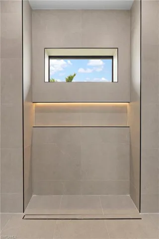 Tiled shower stall featuring a linear drain, recessed niche with accent lighting, and an integrated window