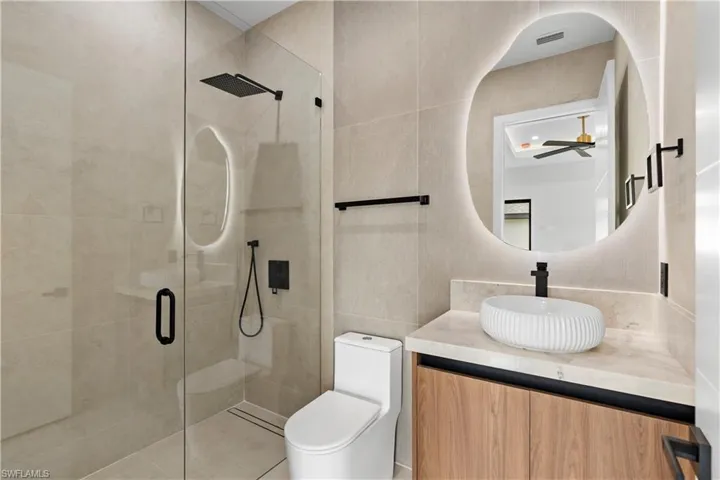 Bathroom featuring a glass-enclosed shower with a black rain showerhead, a floating wood-finish vanity with a vessel sink, and an illuminated irregular-shaped mirror