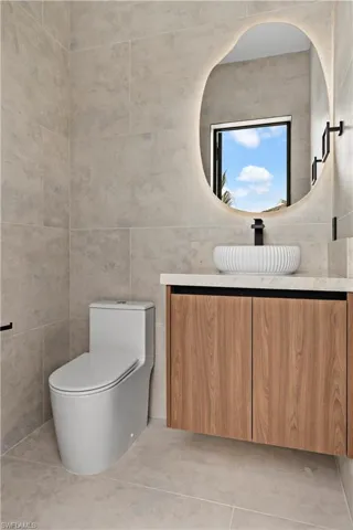 Floating wood-finish vanity with a vessel sink, integrated mirror lighting, and large format wall and floor tiling