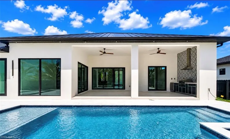 Modern exterior featuring a dark metal roof, clean white stucco finish, and an integrated outdoor kitchen with tile backsplash
