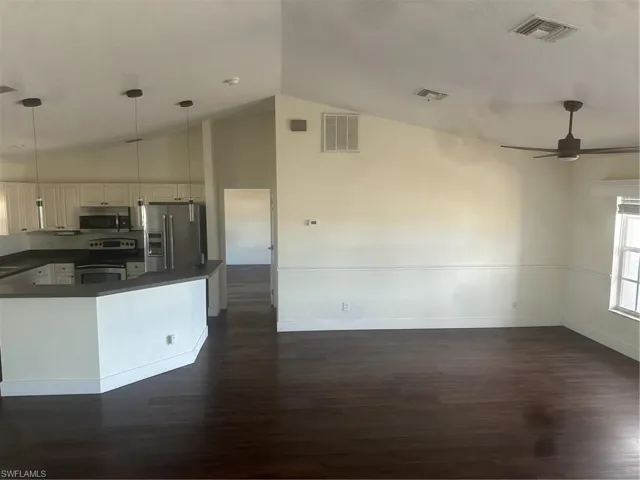 Kitchen featuring dark countertops, hanging light fixtures, refrigerator, dark wood-type flooring, and ceiling fan