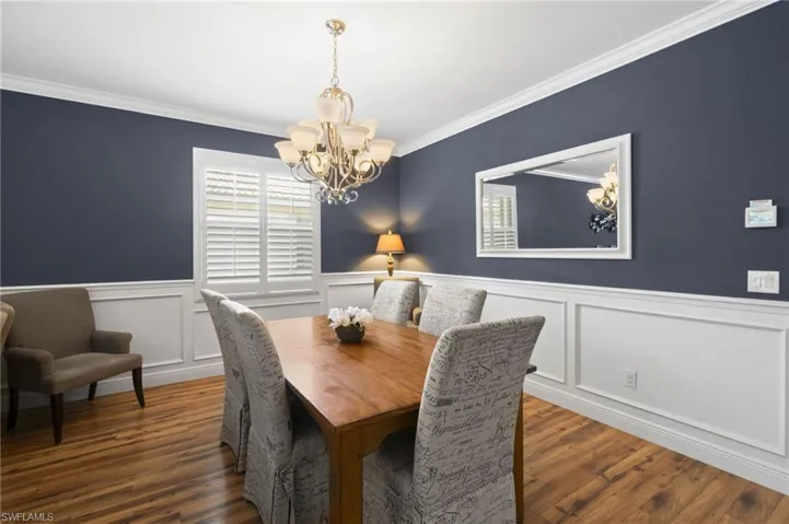 Dining area featuring wood-finish flooring, white wainscoting, white plantation shutters, and a multi-arm chandelier