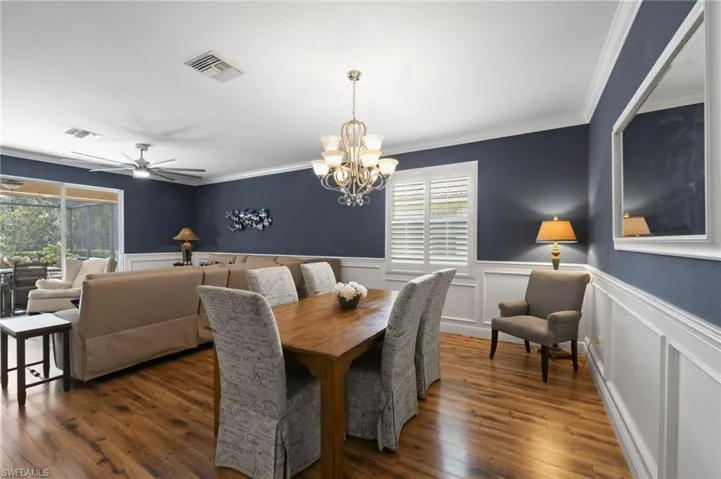 Wood-finish flooring, multi-light chandelier, white wainscoting, plantation shutters, and crown molding