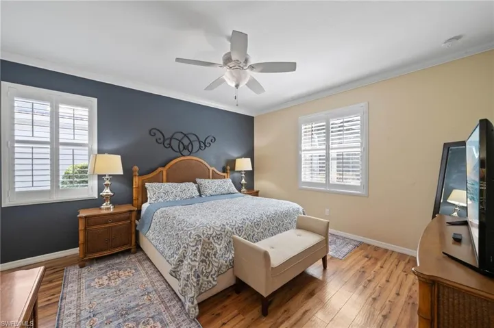 Wood-finish flooring, white plantation shutters, crown molding, and a central ceiling fan