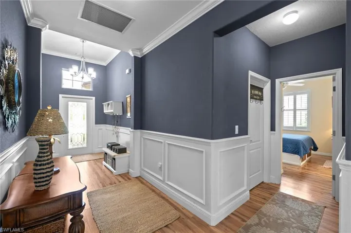 Foyer featuring high ceilings, wood-finish flooring, white wainscoting, a multi-arm chandelier, and a decorative glass-panel front door