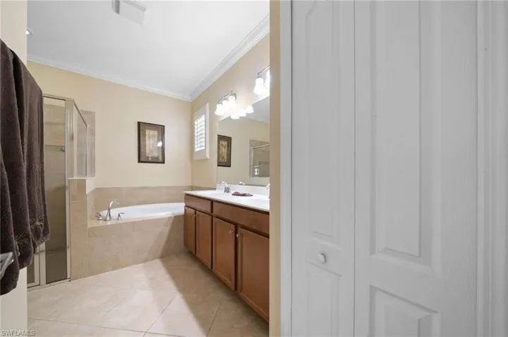 Bathroom featuring a dual-sink vanity with wood cabinetry, a tiled soaking tub, a glass-enclosed shower, and tile flooring