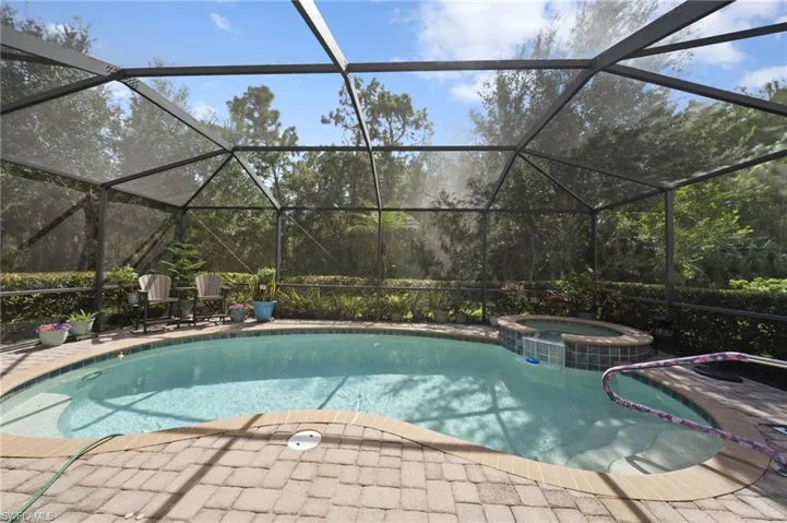 Screened-in pool area featuring a curved swimming pool, integrated spillover spa, brick paver decking, and surrounding privacy landscaping