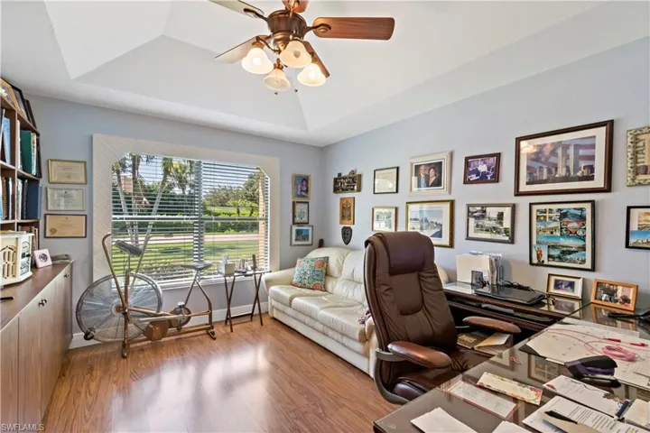 Home office with hardwood / wood-style floors, ceiling fan, and a raised ceiling