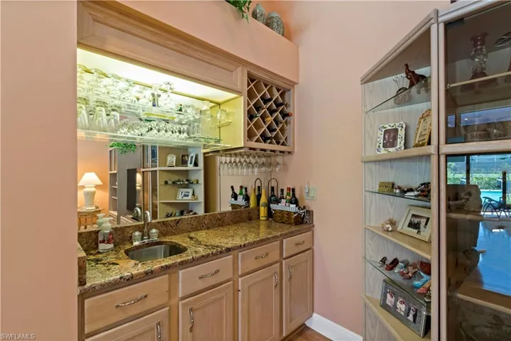 Bar featuring sink, stone countertops, and light brown cabinetry