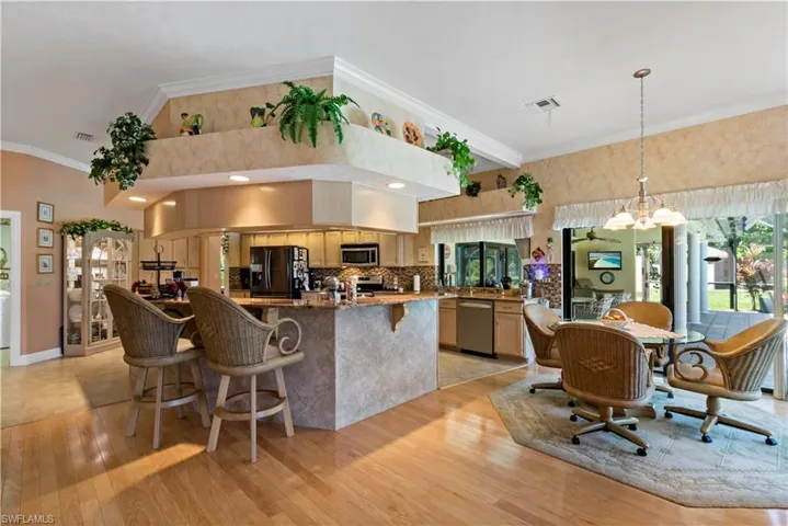 Kitchen with light brown cabinets, tasteful backsplash, stainless steel appliances, light wood-type flooring, and hanging light fixtures