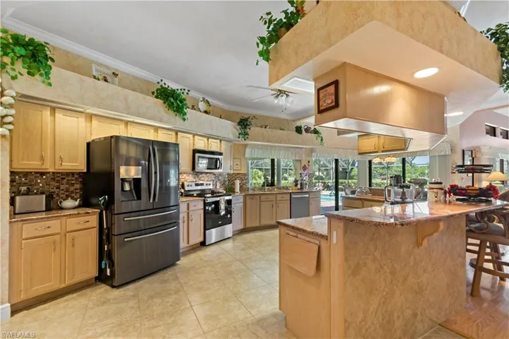 Kitchen with light stone countertops, stainless steel appliances, light tile flooring, backsplash, and ornamental molding