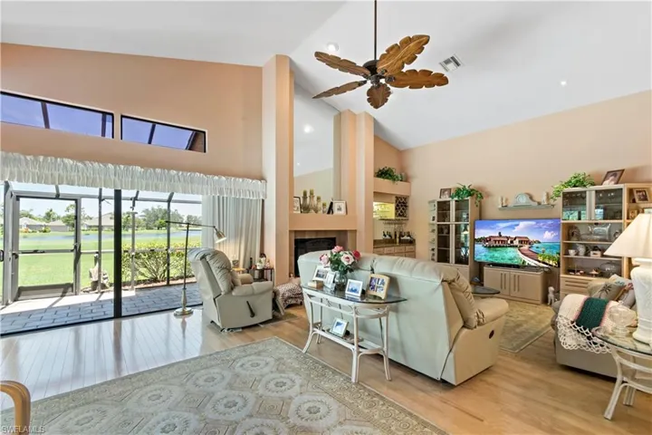 Living room with high vaulted ceiling, wood-type flooring, ceiling fan, and a tile fireplace