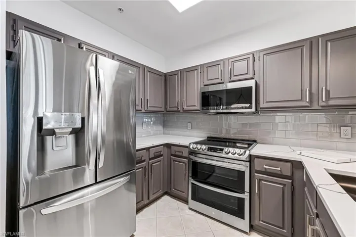 Kitchen featuring light tile patterned flooring, light stone countertops, stainless steel appliances, and backsplash