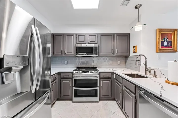 Kitchen featuring tasteful backsplash, light tile patterned floors, light stone countertops, appliances with stainless steel finishes, and sink