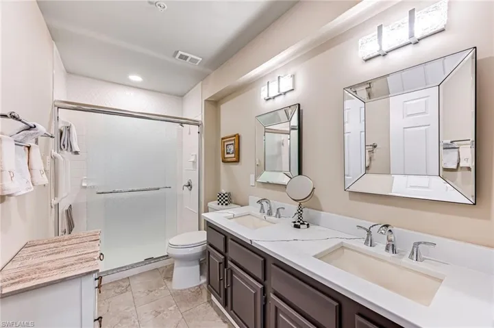 Bathroom with a shower with shower door, toilet, tile patterned flooring, and dual bowl vanity