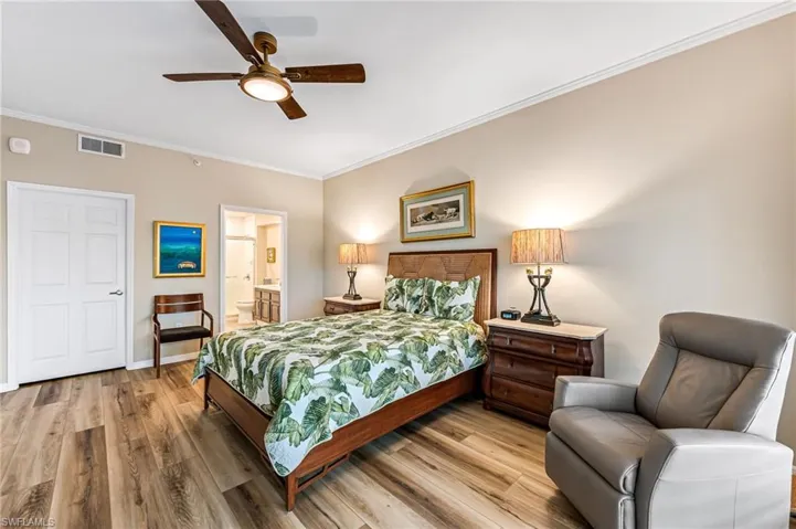 Bedroom with hardwood / wood-style flooring, ornamental molding, ensuite bath, and ceiling fan