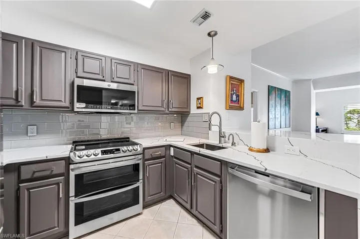 Kitchen featuring stainless steel appliances, decorative backsplash, sink, light stone counters, and light tile patterned floors
