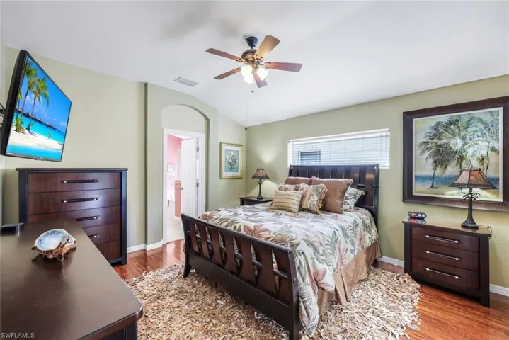 Bedroom featuring light laminate floors, ensuite bathroom, ceiling fan, and vaulted ceiling