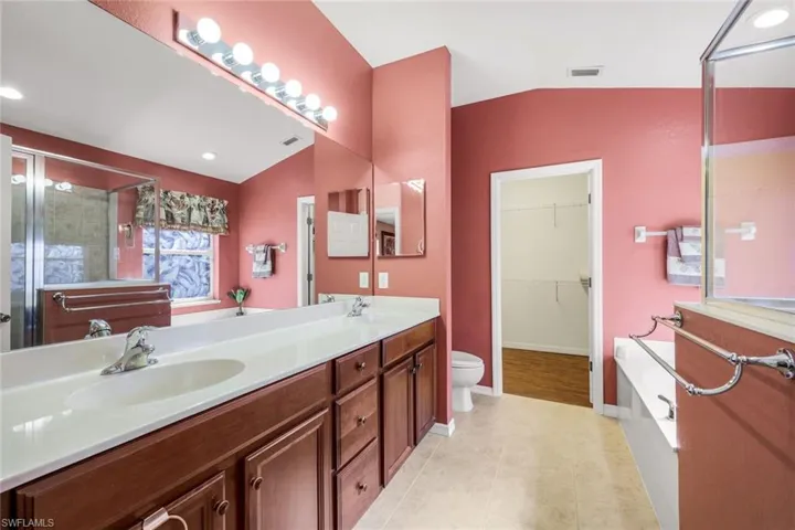 Bathroom featuring lofted ceiling, double vanity, a stall shower, a walk in closet, and a garden tub