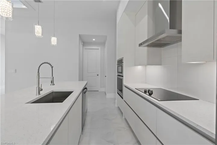 Kitchen featuring modern cabinets, white cabinetry, light stone countertops, and pendant lighting