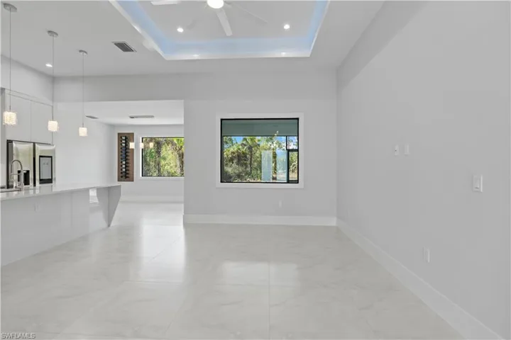 Unfurnished living room with a ceiling fan, a tray ceiling, recessed lighting, and light marble finish flooring
