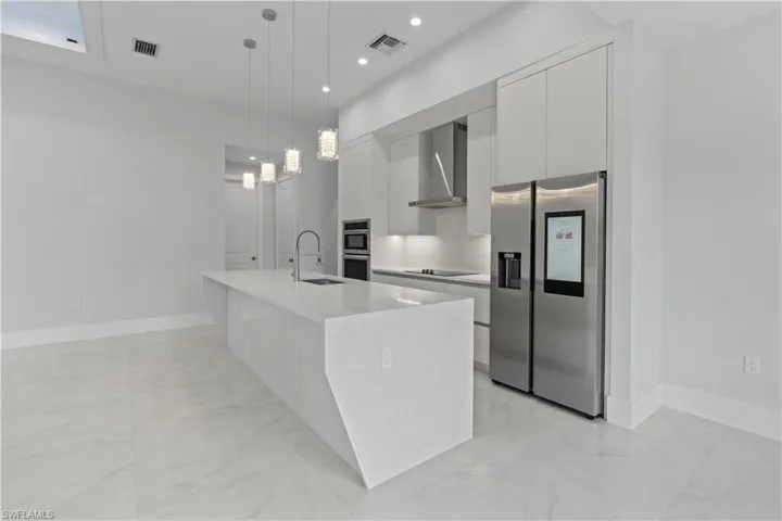 Kitchen featuring modern cabinets, stainless steel appliances, a center island with sink, and light marble finish floors