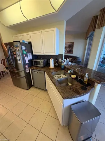 Kitchen featuring white cabinets, appliances with stainless steel finishes, light tile patterned flooring, and a peninsula