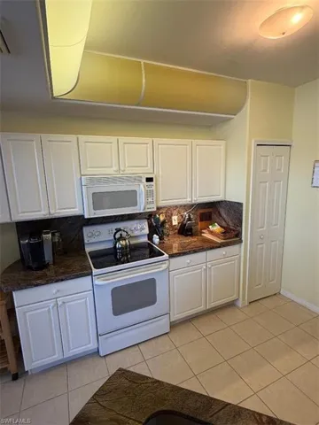 Kitchen with white cabinetry, white appliances, light tile patterned floors, and dark stone countertops