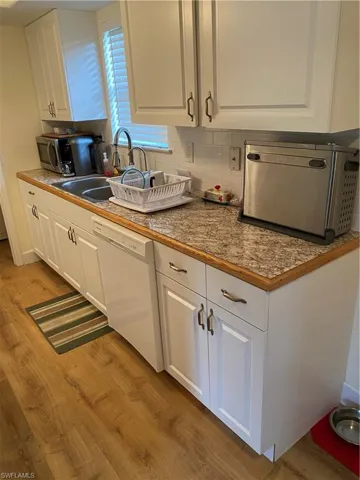 Kitchen with white cabinetry, tasteful backsplash, dishwashing machine, and light hardwood / wood-style flooring