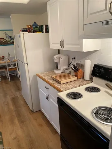 Kitchen featuring decorative backsplash, white cabinetry, stove, and light wood-type flooring