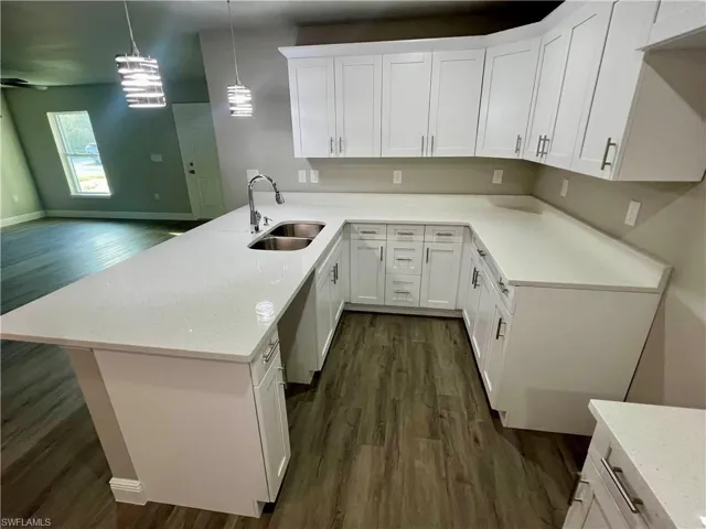 Kitchen featuring sink, white cabinetry, hanging light fixtures, dark hardwood / wood-style flooring, and kitchen peninsula