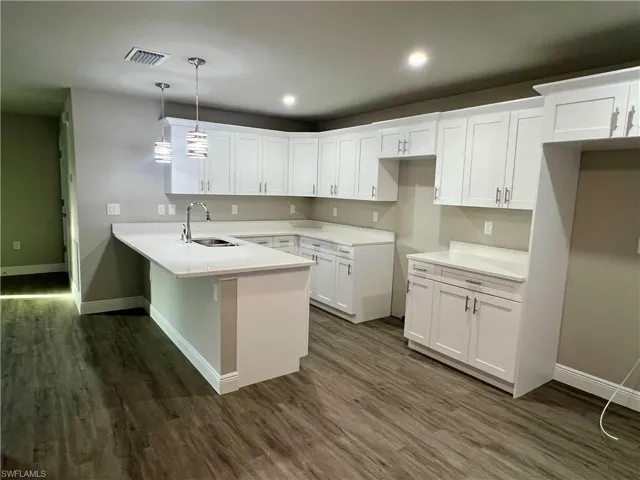 Kitchen featuring dark wood-type flooring, sink, hanging light fixtures, kitchen peninsula, and white cabinets