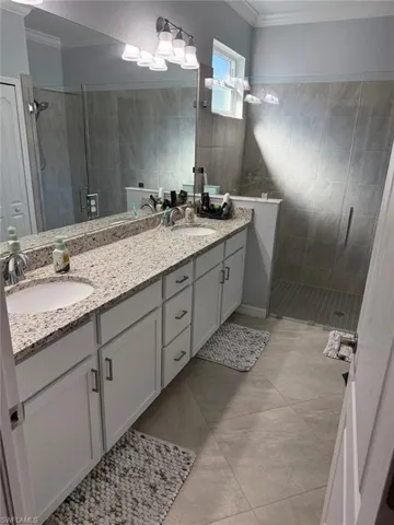 Full bath featuring a shower stall, ornamental molding, a textured wall, and double vanity