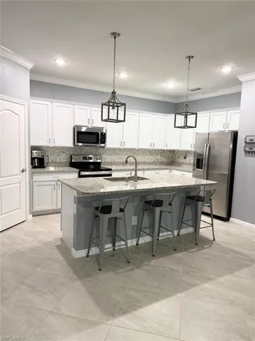 Kitchen featuring a kitchen bar, a kitchen island with sink, stainless steel appliances, white cabinets, and crown molding