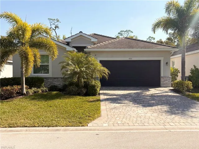 View of front of property featuring stone siding, decorative driveway, stucco siding, and a front yard