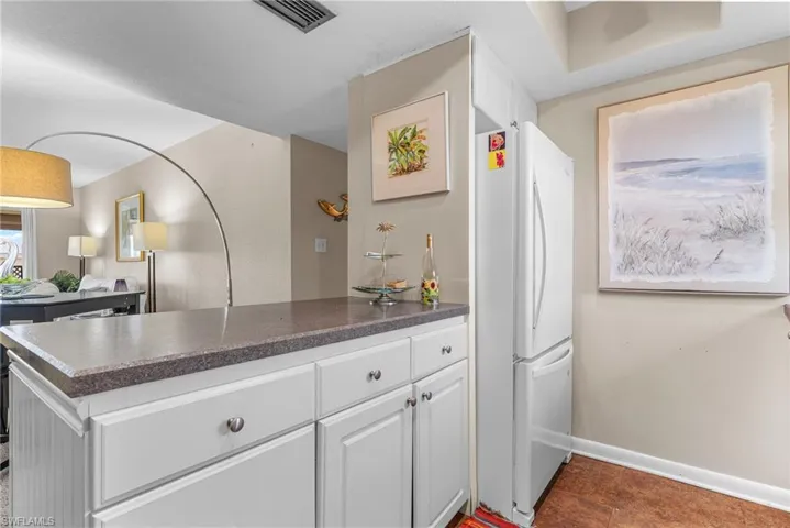 Kitchen with dark countertops, freestanding refrigerator, white cabinets, and a peninsula