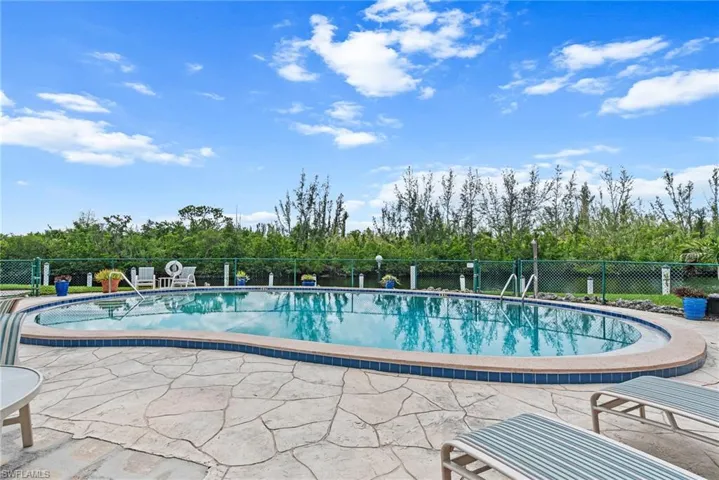 Community pool featuring view of wooded area and a patio area
