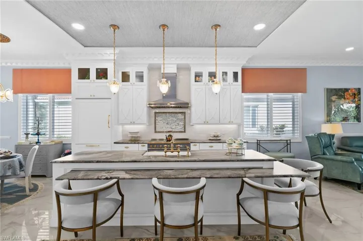 Kitchen with hanging light fixtures, wall chimney exhaust hood, white cabinetry, and decorative backsplash