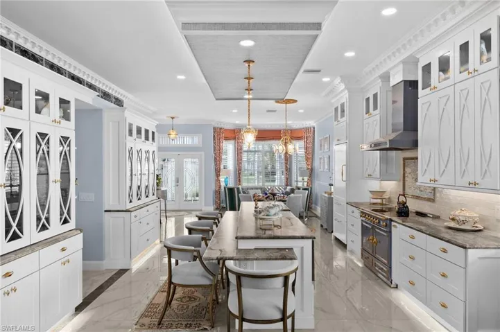 Kitchen featuring a kitchen bar, a center island, wall chimney range hood, pendant lighting, and dark stone countertops