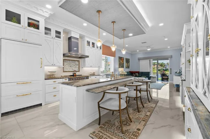 Kitchen with white cabinetry, a kitchen breakfast bar, hanging light fixtures, a kitchen island, and wall chimney range hood