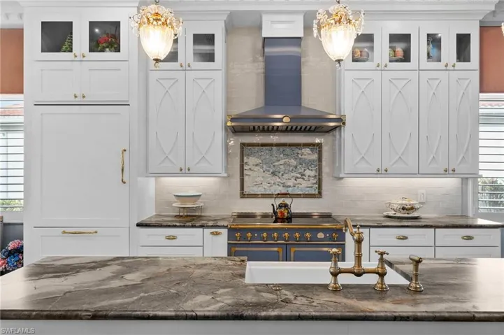 Kitchen with backsplash, white cabinetry, decorative light fixtures, and wall chimney exhaust hood